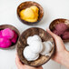 A person holding a bowl of yellow Pitaya Foods coconut sorbet with a scoop of yellow coconut sorbet on top.