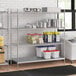 Stainless steel wire shelf kit with solid stainless steel bottom shelving unit with food containers on it.