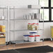 A Regency chrome wire shelving unit in a kitchen with white and blue containers on the bottom shelf.