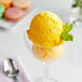 A clear bowl of yellow Pitaya Foods Organic Passion Fruit Sorbet with a spoon and a mint leaf.