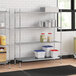 A metal Regency wire shelving unit in a professional kitchen with white and blue plastic containers on the shelves.