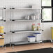 A Regency galvanized steel shelving unit in a professional kitchen with containers and buckets on the shelves.