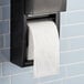 A Charmin Essentials Mega Roll of 2-ply toilet paper on a black toilet paper holder.