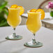 Two glasses of Oregon Fruit In Hand tangerine puree with orange slices on top on a table.