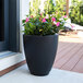 A Mayne Caprio black planter with a potted plant with pink flowers.