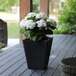 A black Mayne Bristol planter with white flowers on a deck table.