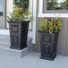 Two Mayne black planters with plants in them on a patio table.