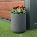 A Mayne Arden graphite gray round planter with flowers in it on the grass.