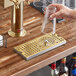 A hand holding a glass over a Regency gold surface-mount beer drip tray.