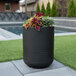 A black Mayne Arden round planter with plants in it on a grassy area.