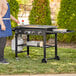 A woman wearing a blue apron standing next to a Backyard Pro outdoor griddle on a table.