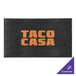 A black M+A Matting ColorStar Impressions custom logo mat with orange text that says "Taco Casa" on a table.