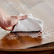 A person's hand using a white Monarch Brands bar towel to wipe a table.