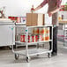 A man using a Lakeside stainless steel utility cart in a professional kitchen.