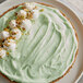 A green pistachio pudding pie with white frosting and nuts.