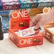 A hand taking a ONE Peanut Butter Cup Protein Bar package from a box.