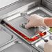 A person using a Choice stainless steel slotted pan cover to put carrots in a food container.