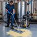 A person using a Goodway stainless steel wet/dry vacuum to clean a floor in a professional kitchen.