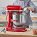 A woman using a red KitchenAid bowl lift mixer with a silver bowl.