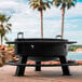 An Old Country BBQ Pits steel round fire pit with handles on a stone surface.