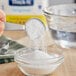 A measuring spoon with white powder being poured into a bowl.