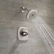 A Delta stainless steel shower trim kit with a metal knob and a shower head with water running out of it.