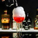 A hand using a Flavour Blaster to pour red liquid into a glass with a skull on it.