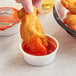 A person dipping a chicken wing into a small container of Heinz Hot Buffalo Sauce.