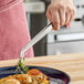 A hand using Mercer Culinary curved precision tongs to plate scallops.