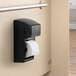 A Scott black vertical double roll toilet paper dispenser on a wall with rolls of toilet paper.