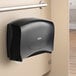 A black double jumbo roll horizontal toilet paper dispenser on a wall.