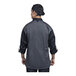 A chef wearing a black Uncommon Chef Roma long sleeve chef coat with a silver and grey mesh back.