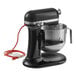 A black and silver KitchenAid mixer with a red cord.