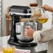 A person pouring yellow liquid into a bowl in a KitchenAid commercial mixer.