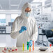 A man in a white protective suit and gloves pouring liquid into test tubes.