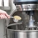 A person pouring grain into an Avantco planetary floor mixer.