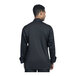 The back view of a man wearing a black Uncommon Chef long sleeve chef coat with black mesh.