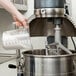 A person pouring liquid from a measuring cup into an Avantco floor mixer.