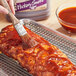 A hand holding a paint brush over a rack of ribs with Kraft Hickory Smoke BBQ Sauce.