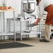 A man in an apron and hat working on a Regency stainless steel mixer table.