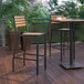 A Flash Furniture Lark Natural Faux Teak Slat stackable barstool on a wooden deck with a table and chairs.