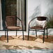 Two Flash Furniture medium brown rattan arm chairs on a rug outside.