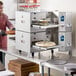 A man in a kitchen with a Cooking Performance Group double stacked countertop impinger conveyor oven.