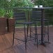 A black Flash Furniture Lila stackable bar stool on a deck with a table.