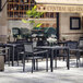 A Flash Furniture black polyresin slat arm chair on a table on a patio.