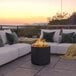 A Flash Furniture black steel fire pit on a table in an outdoor patio with a fire burning in it.