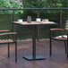 A Flash Furniture natural faux teak table with a black steel frame on a wooden deck with chairs.