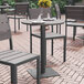 A Flash Furniture round faux teak table and chairs on a brick patio with a wine glass on the table.