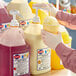 A person in gloves pouring Hartley's Mantecado snow cone syrup from a yellow jug into a cup.