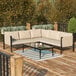 A Flash Furniture black steel sectional with beige cushions on an outdoor patio with a glass table.